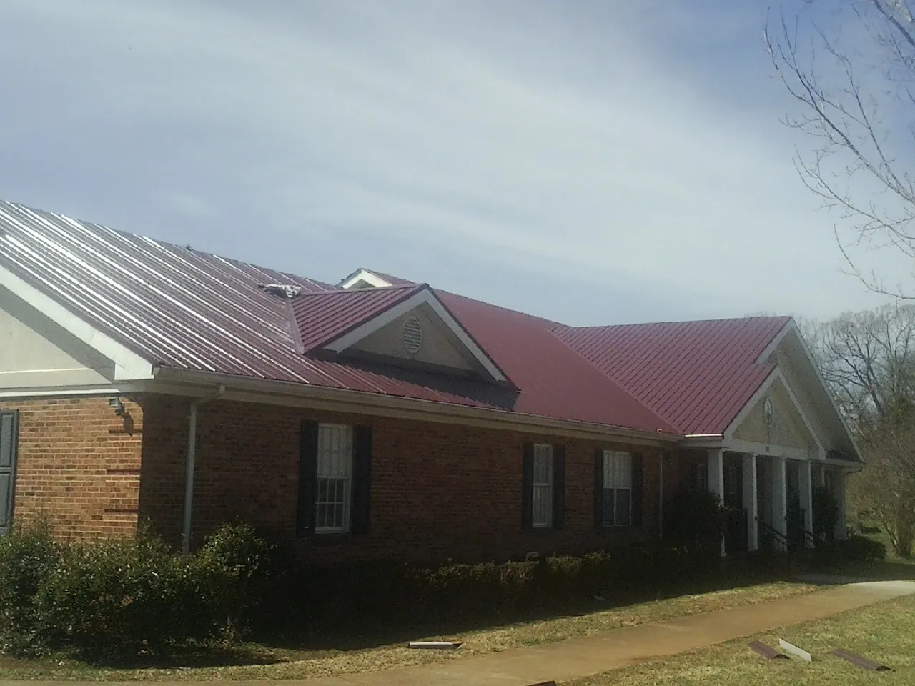 Red metal roof with gabled entries on a long brick building, from a Hail Damage Roof Repair job in Pahrump