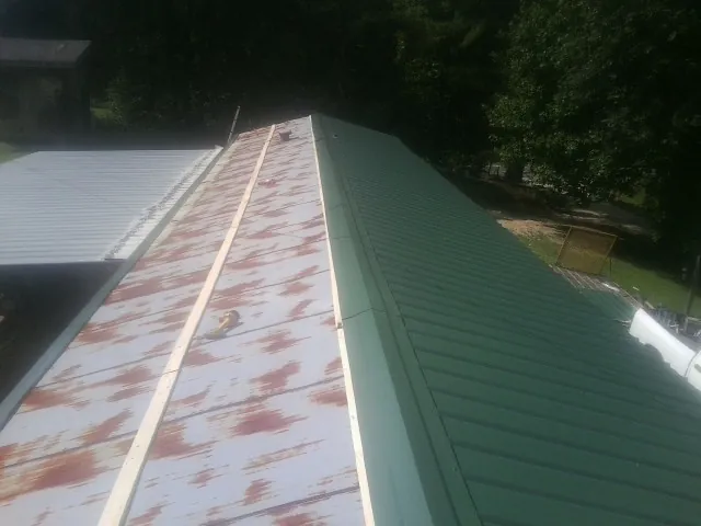 Old rusted panels beside newly installed green metal roofing — Wind Damage Roof Repair by Roofing Brothers in Pahrump