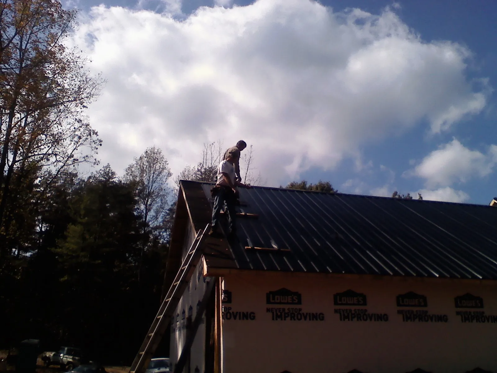 Roofer fastening dark metal panels high against a cloudy sky, from a Roof Inspection job in Pahrump