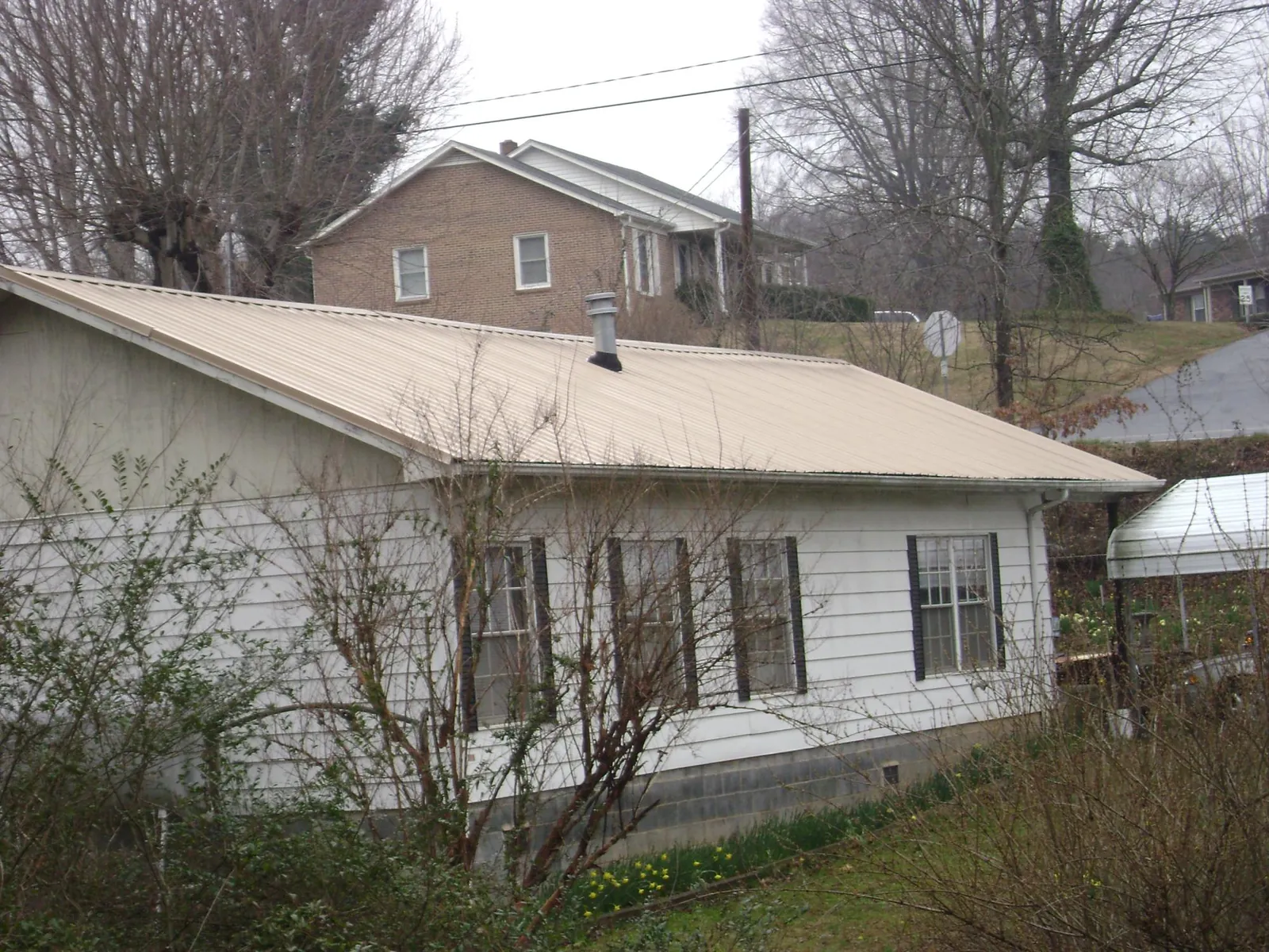 Tan metal roof on a white sided house set into a hillside — Commercial Roofing by Roofing Brothers in Pahrump